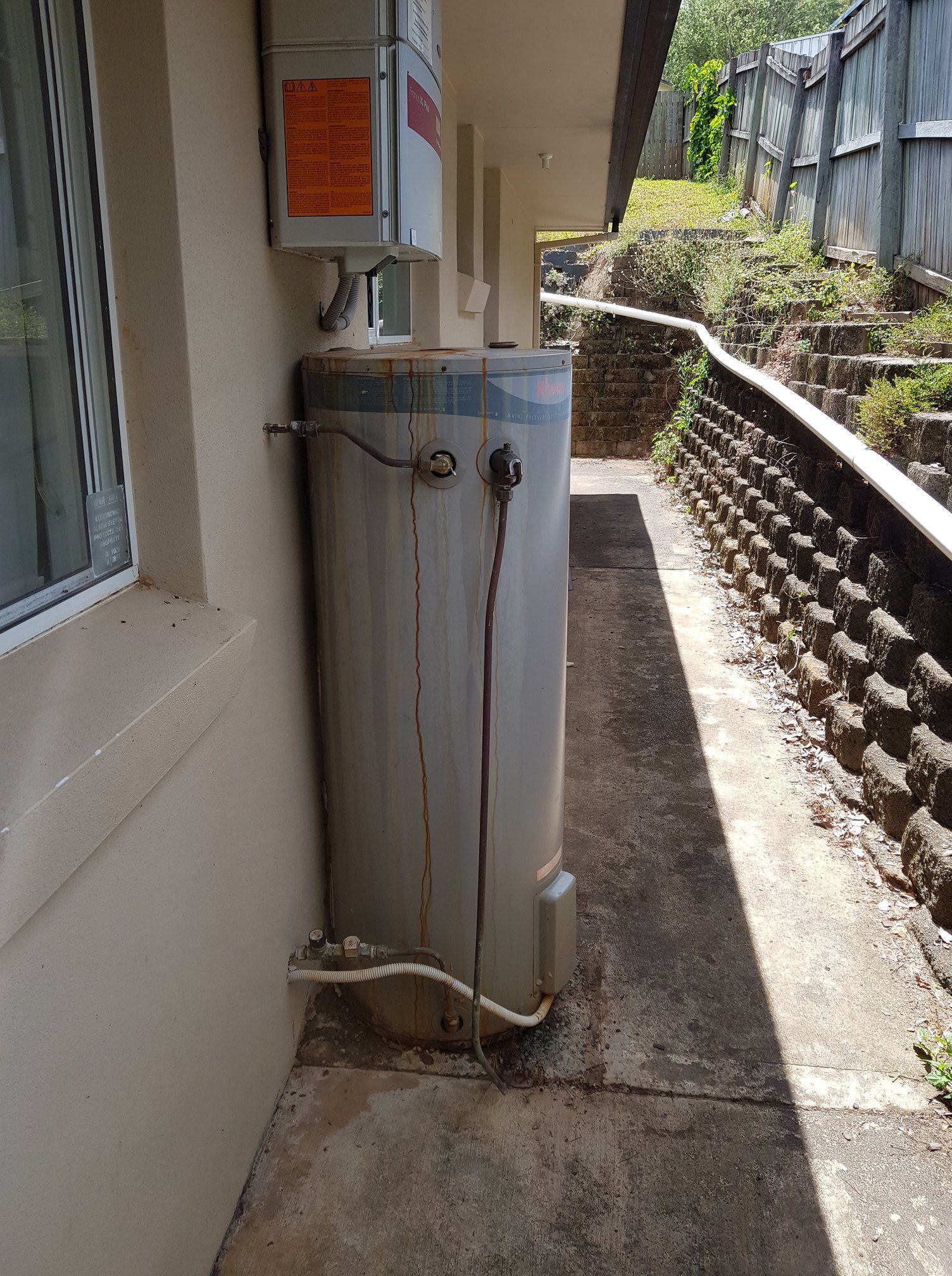 Exterior of a Water Heater on a Concrete Walkway Next to a Building — 24/7 Hot Water in Valdora, QLD