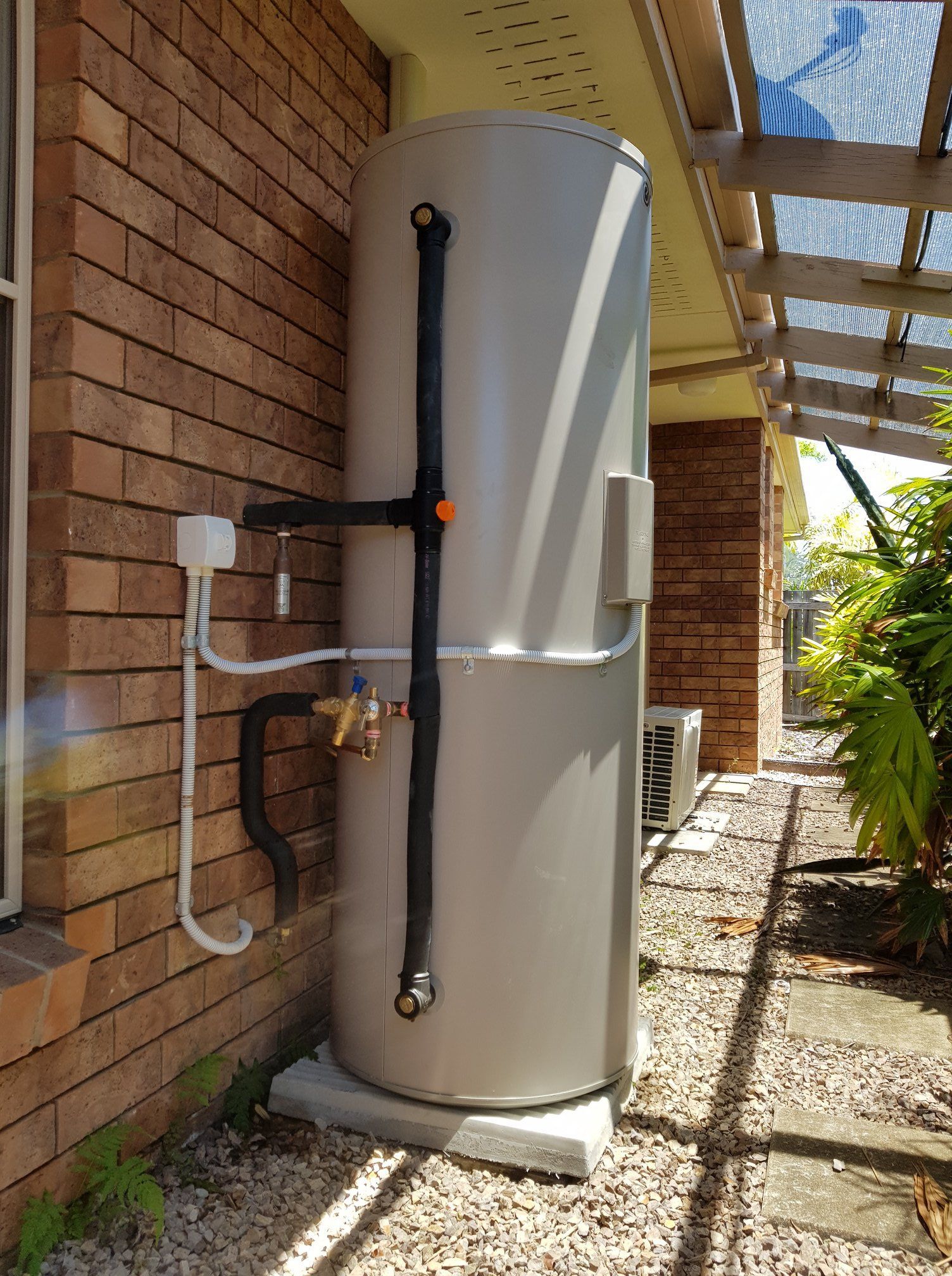 a Cylindrical, Gray Water Heater Attached to a Brick Wall — 24/7 Hot Water in Gympie, QLD