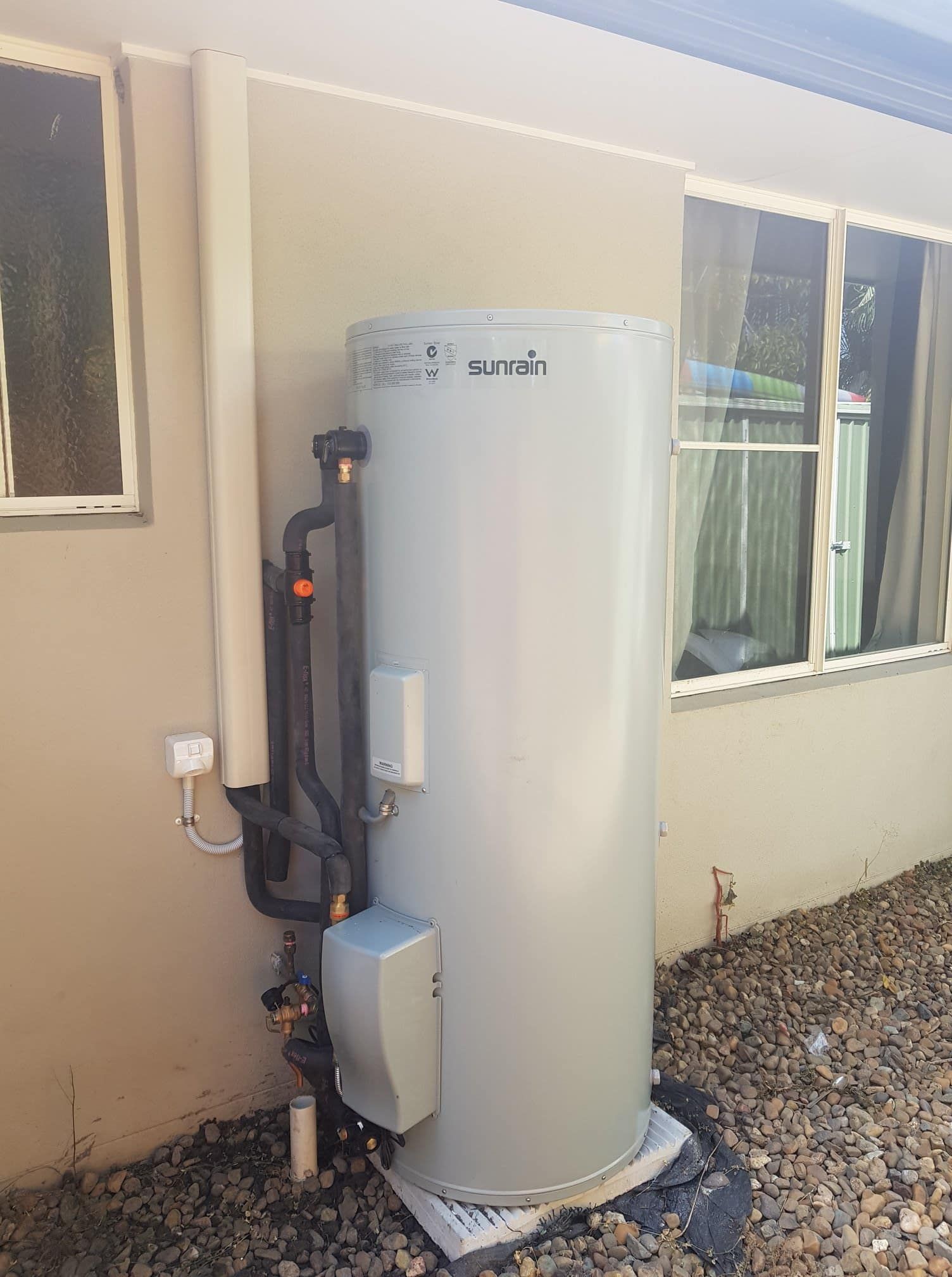 Tall, cylindrical hot water heater against a beige wall, with black pipes and a control box. — 24/7 Hot Water in Caloundra, QLD
