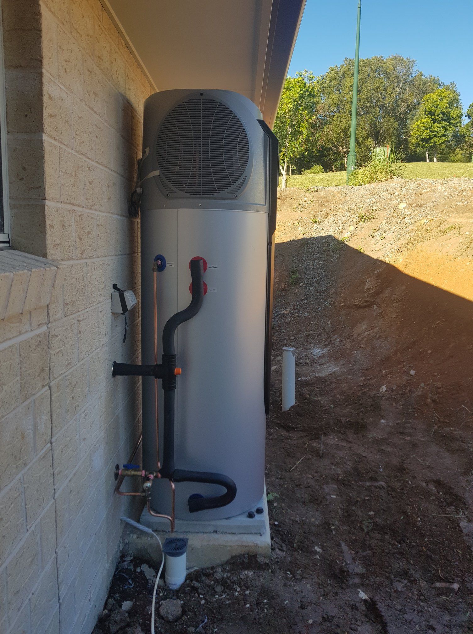 Heat Pump Water Heater Mounted on a Concrete Slab Next to a Building — 24/7 Hot Water in Valdora, QLD