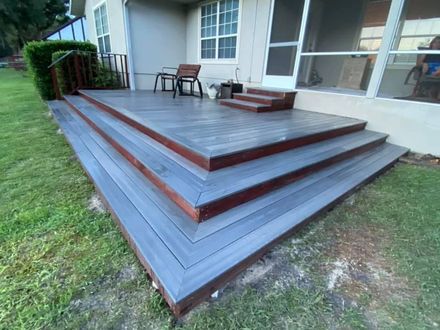 A person in work clothes and gloves uses a power drill to install wooden planks on a fence outdoors. A person in work clothes and gloves uses a power drill to install wooden planks on a fence outdoors.