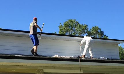 A hand uses a textured roller to apply tan paint to a rough, light-colored exterior wall. A hand uses a textured roller to apply tan paint to a rough, light-colored exterior wall.
