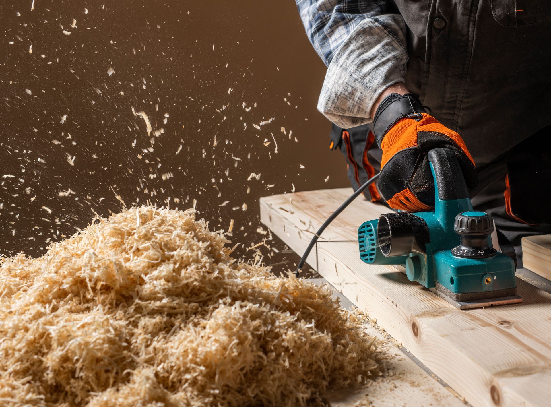 A woodworker uses an electric power planer on a wooden board, creating a large pile of sawdust shavings. A woodworker uses an electric power planer on a wooden board, creating a large pile of sawdust shavings.