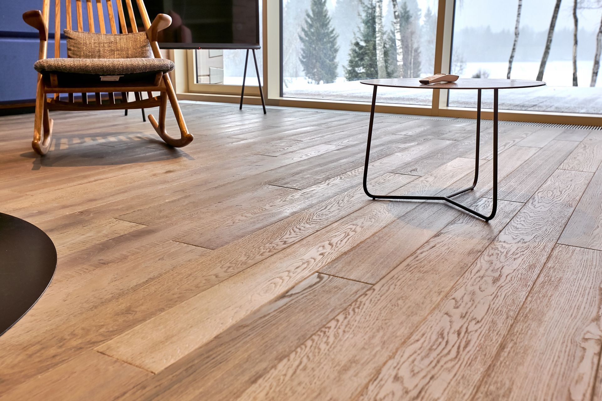 Two people installing wood-look laminate flooring panels on a white underlay, with a utility knife nearby.