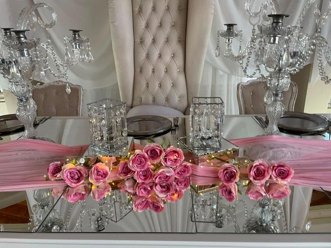 Elegante mesa decorada en rosa y plata con centro de mesa floral, mesa con espejo y detalles de cristal.