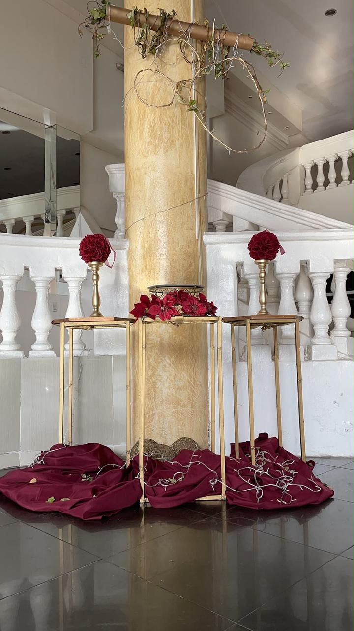 Escenario nupcial floral en tonos dorados y burdeos con tela drapeada y fondo de escalera blanca.