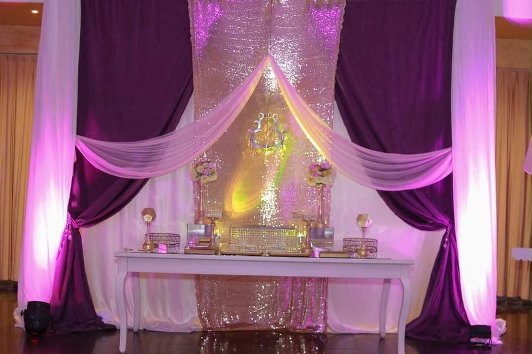 Altar iluminado con luz púrpura, adornado con telas, velas y flores decorativas en un escenario para eventos formales.