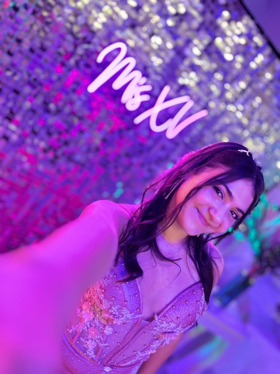 Mujer tomándose una selfie bajo luces de neón moradas con un fondo brillante y un letrero de