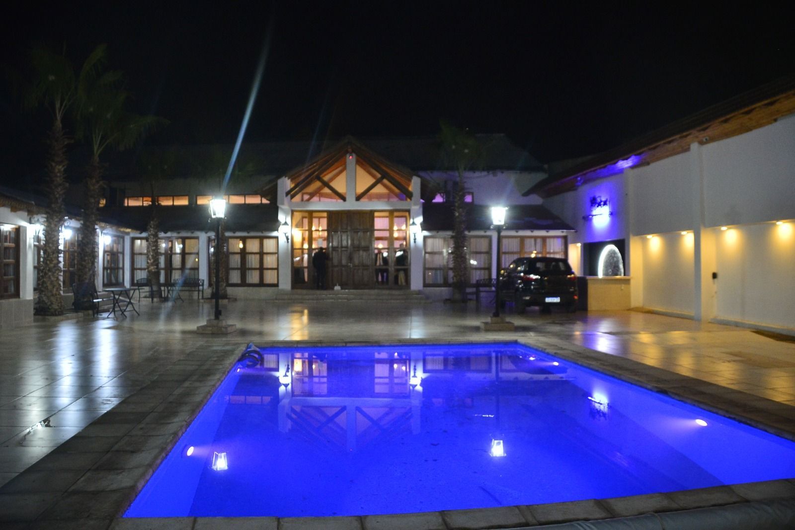 Patio nocturno del complejo turístico con una piscina azul brillante y edificios iluminados al fondo.