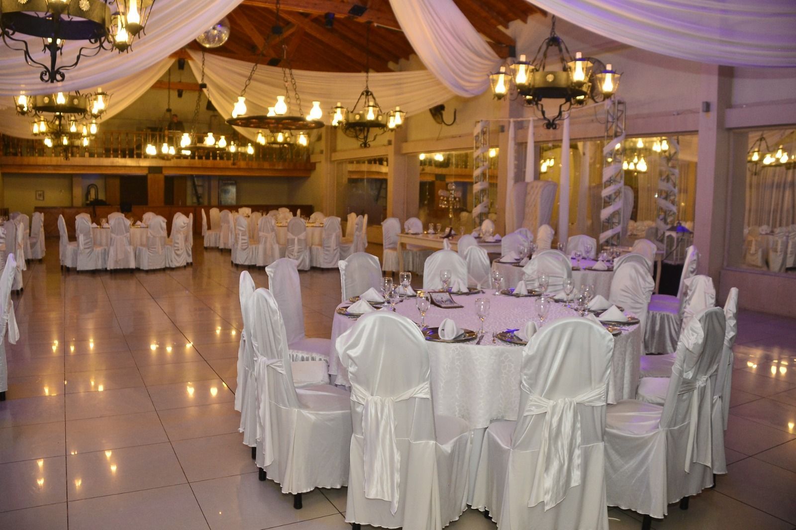 Elegante salón de banquetes con mesas, sillas y candelabros cubiertos con manteles blancos.