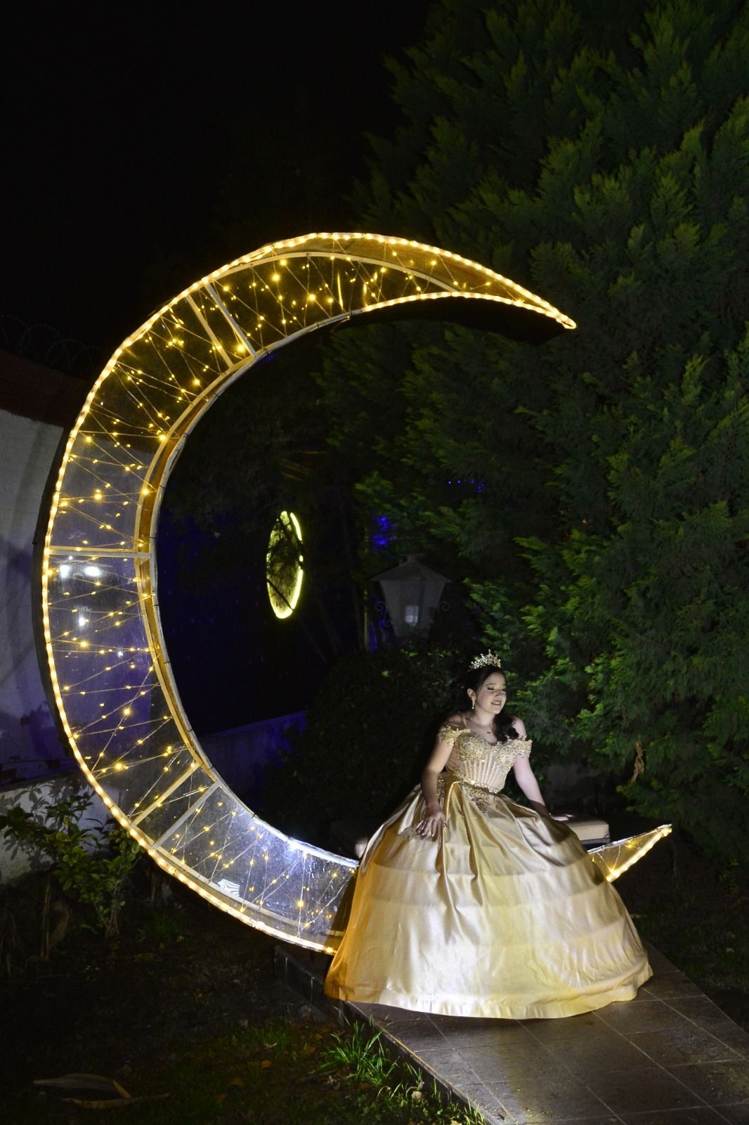 Mujer con un vestido blanco junto a una escultura de luna creciente resplandeciente por la noche.