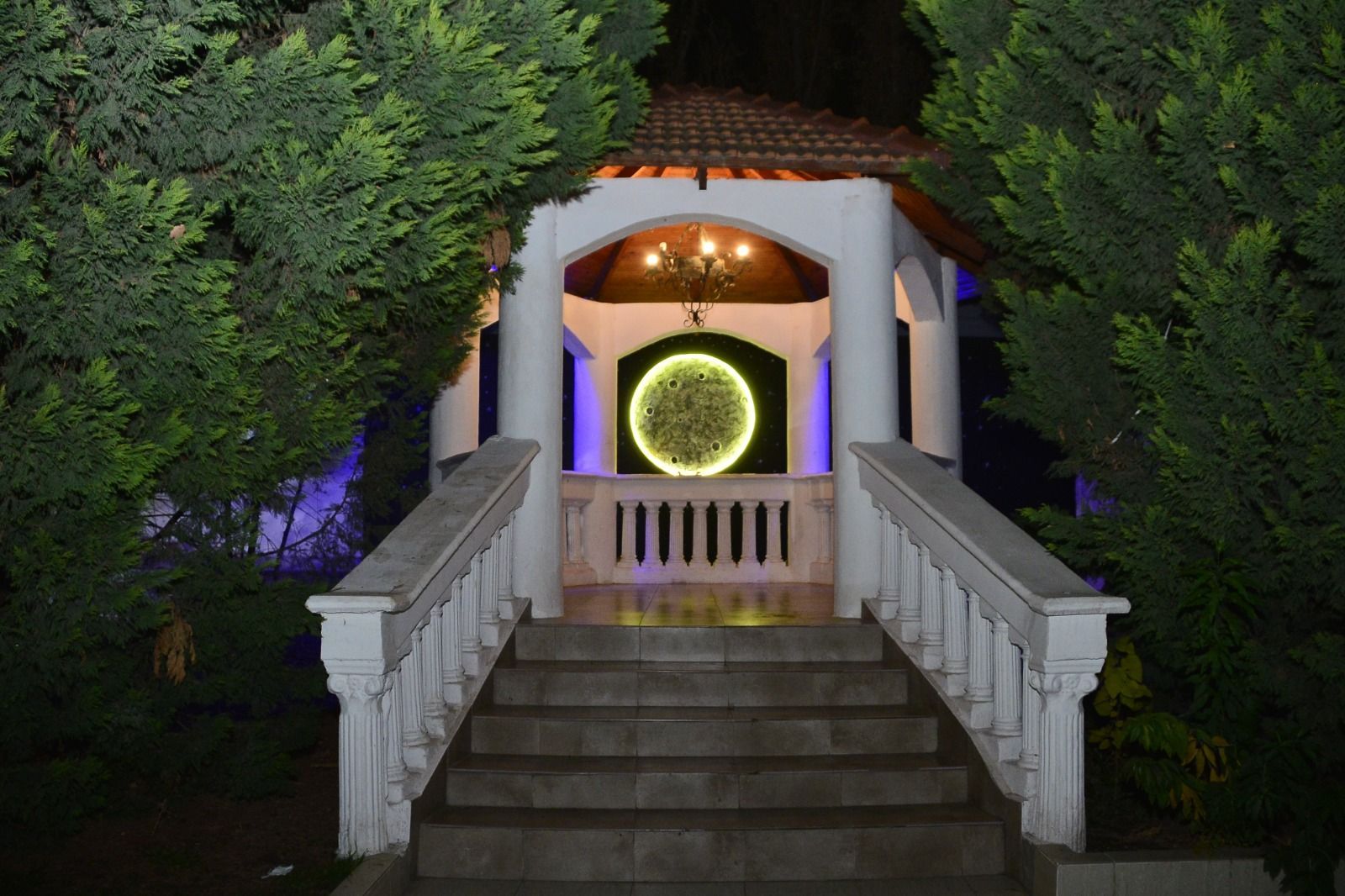 Escalera de piedra iluminada que conduce a la entrada de un pequeño santuario iluminado, rodeado de una densa vegetación.