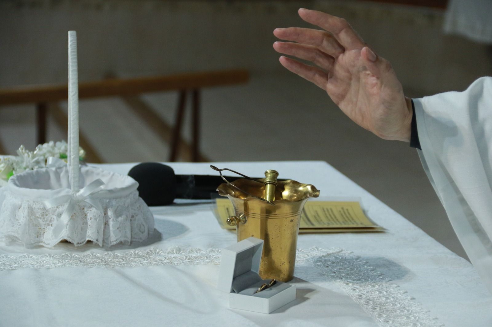 Mesa del altar con cáliz y pan de comunión, mano del sacerdote alzada en señal de bendición.