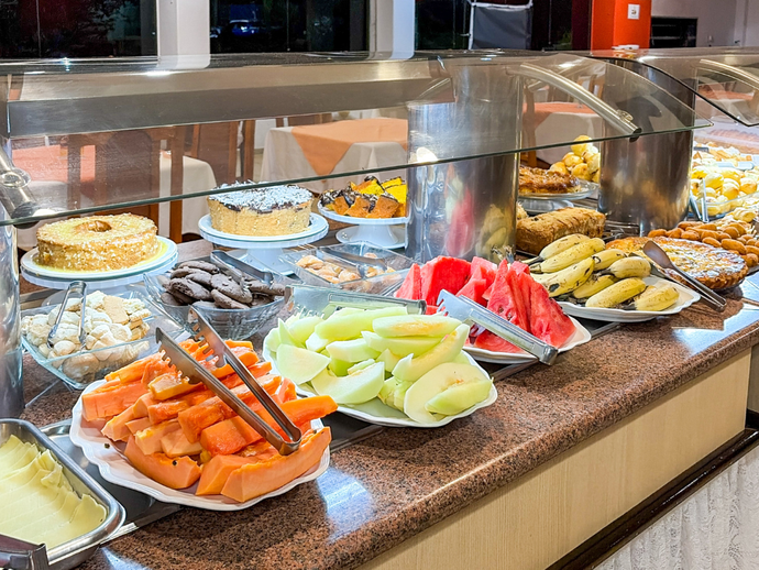 Balcão de buffet com frutas variadas, frutos do mar e sobremesas sob vitrine de vidro.