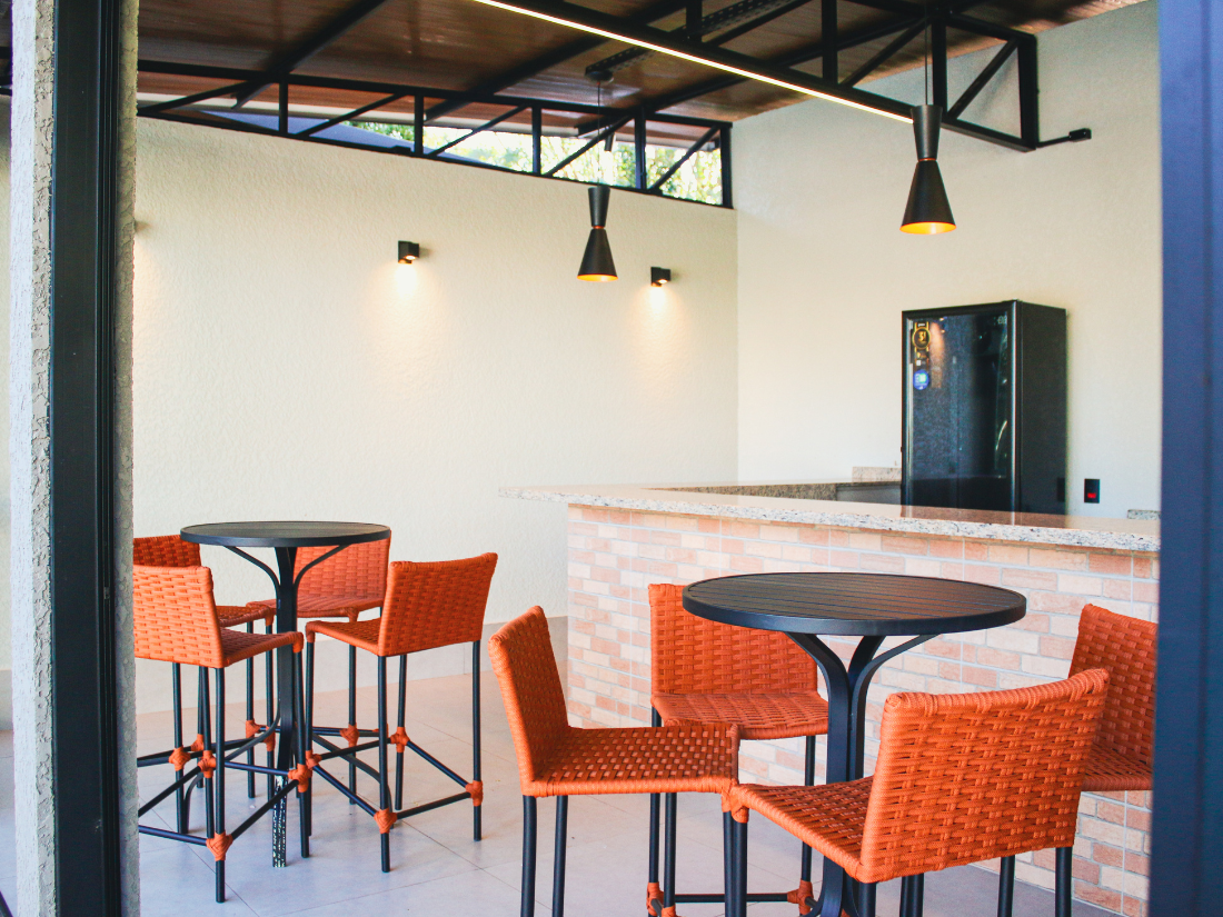 Interior de café moderno com cadeiras laranja, mesas redondas e balcão de bar branco.