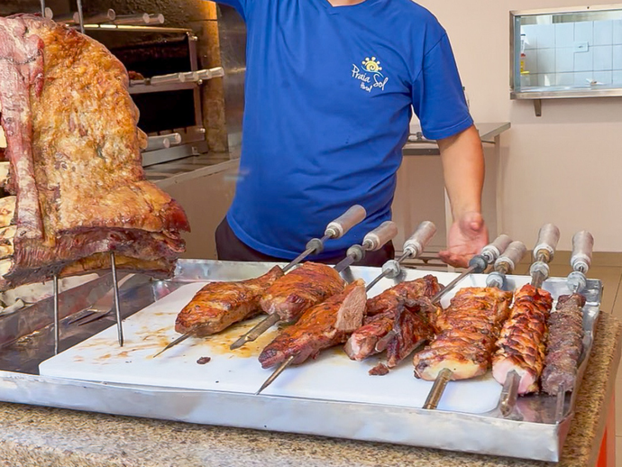 Pessoa servindo carne assada em uma barraca de comida, com espetos e um grande assado em exposição.
