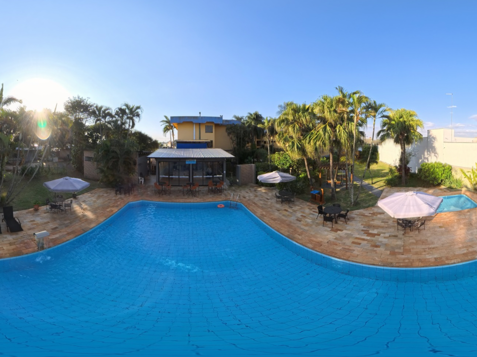 Piscina no quintal com água azul, espreguiçadeiras, guarda-sóis, palmeiras e uma casa ao fundo.