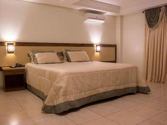Cama arrumada num quarto de hotel bege com apliques de parede e cortinas.