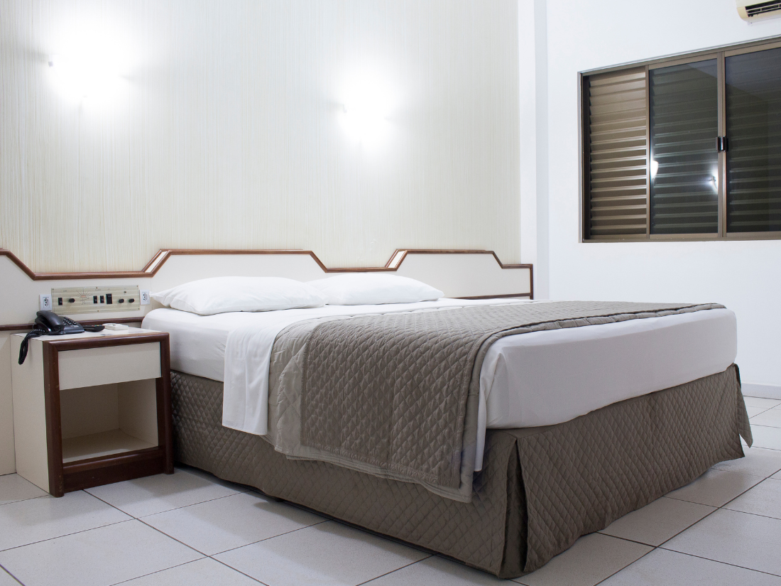 Quarto minimalista com cama, mesa de cabeceira, piso de azulejo e persianas.