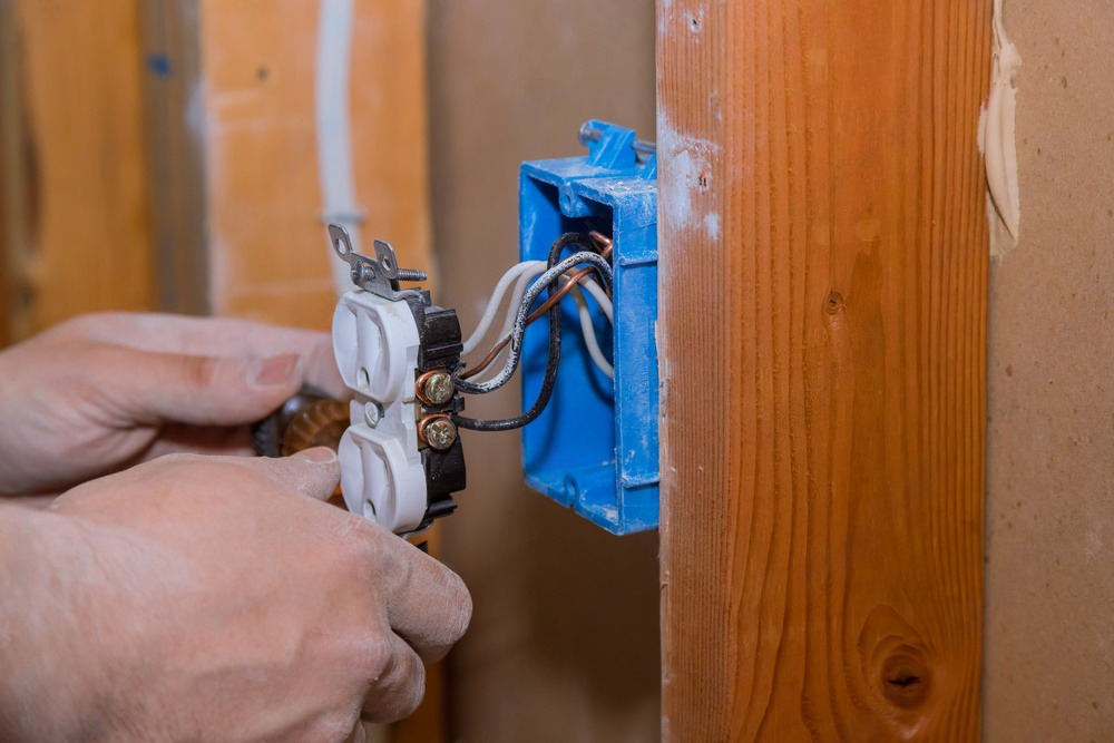 A person is installing an electrical outlet in a wooden wall.