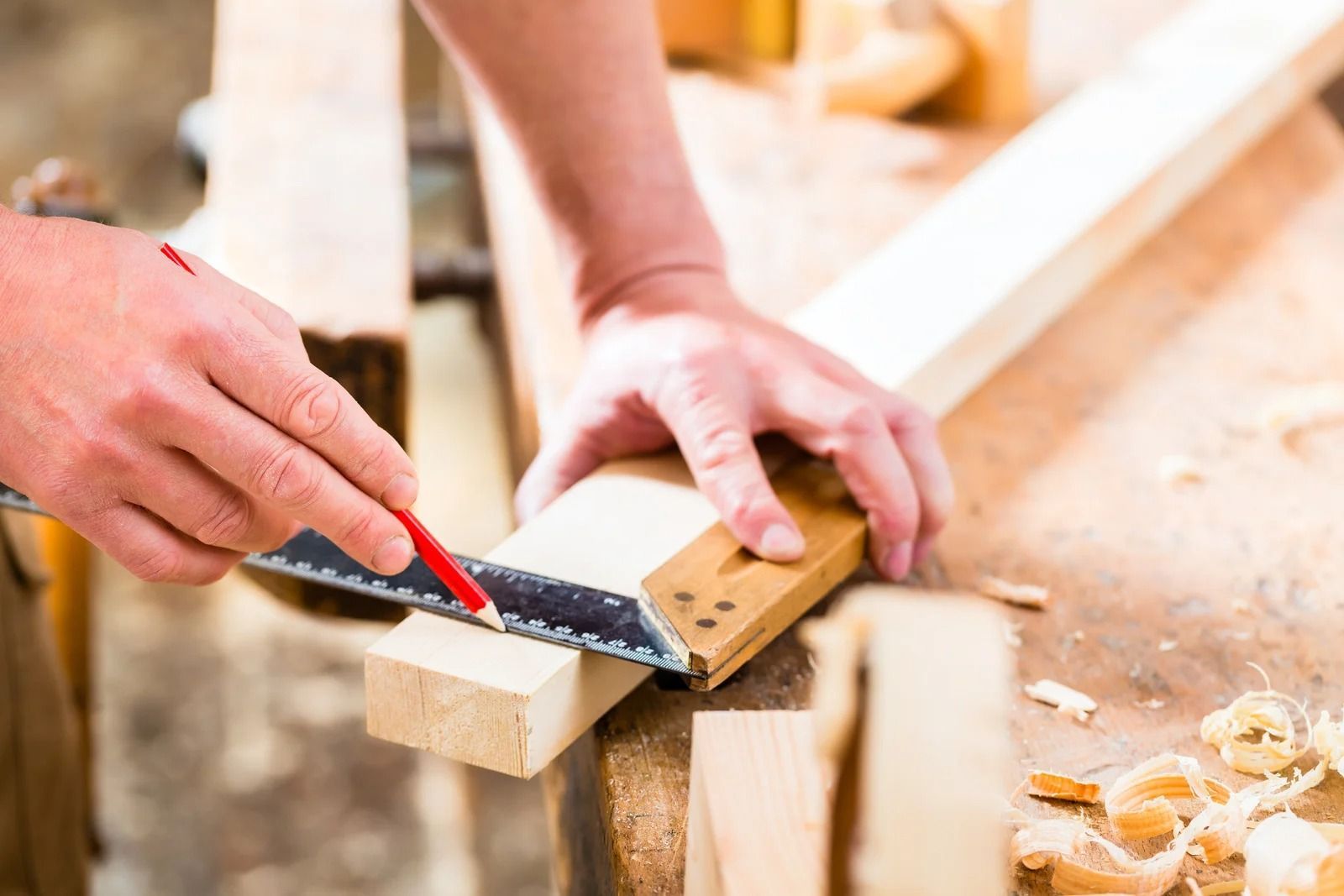 Hands using a hand saw to cut wood on a workbench in a workshop