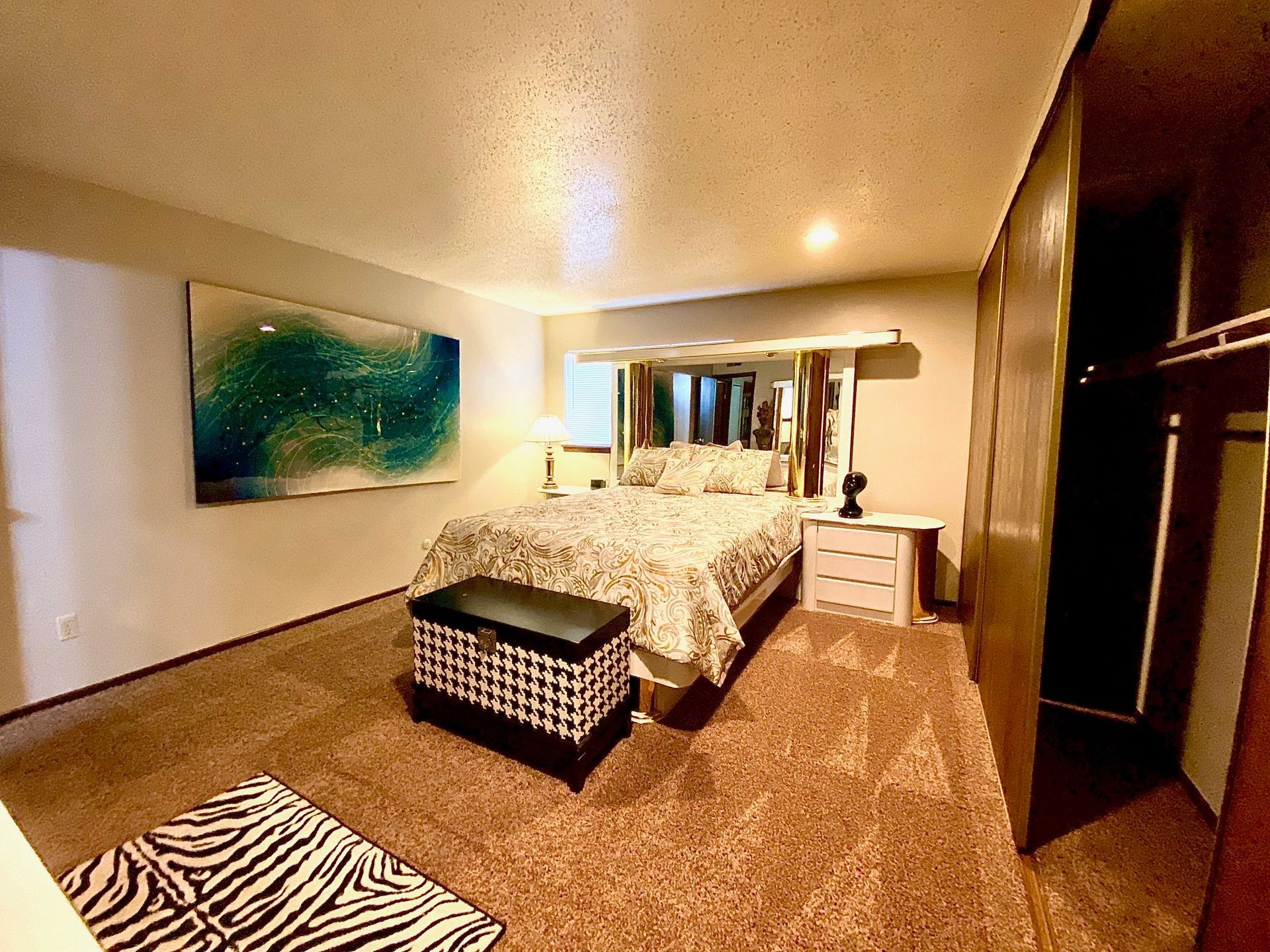 Bedroom with bed, art, rug, nightstand, and wardrobe. Earth-toned decor.