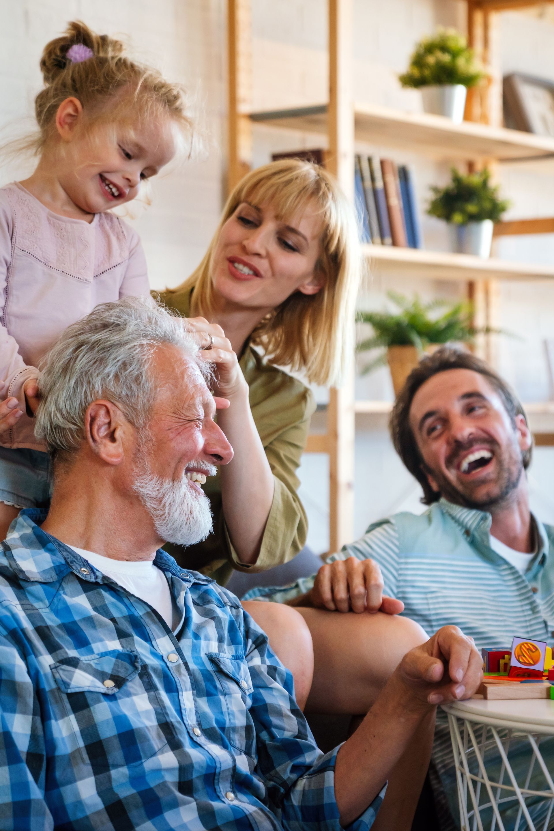 Family smiling together in a cozy living room, with a child leaning toward an older man in a blue plaid shirt.