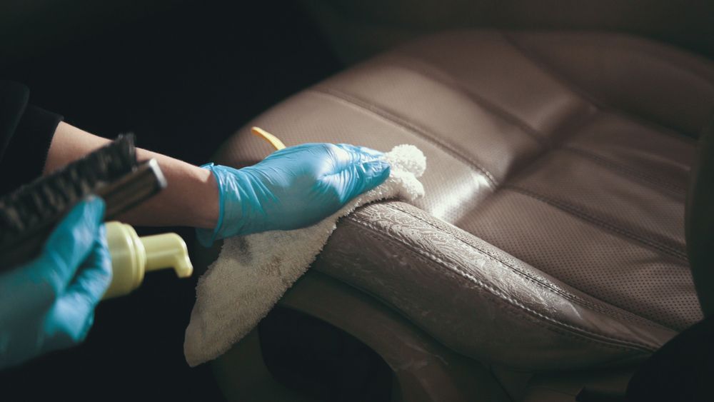 A Person Wearing Blue Gloves is Cleaning a Leather Seat in a Car — Furniture & Auto Pride in Port Macquarie, NSW