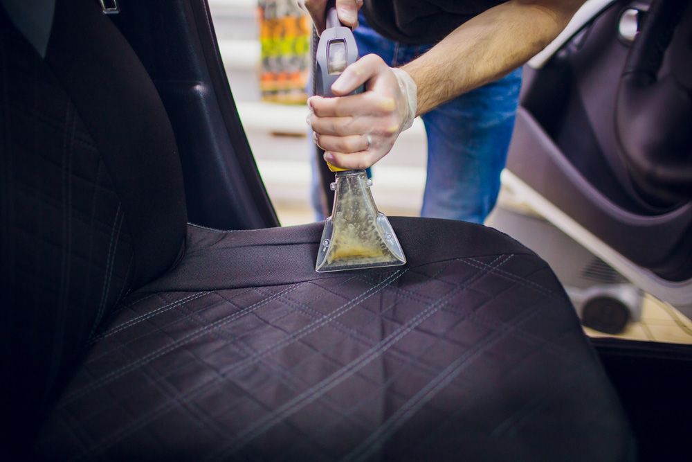 A Man is Cleaning the Back Seat of a Car With a Vacuum Cleaner — Furniture & Auto Pride in Forster, NSW