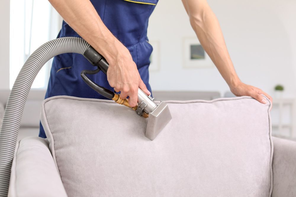 A Man is Cleaning a Couch With a Vacuum Cleaner — Furniture & Auto Pride in Taree, NSW