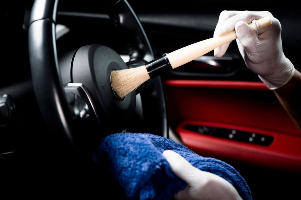 A Person is Cleaning the Steering Wheel of a Car With a Brush — Furniture & Auto Pride in Forster, NSW