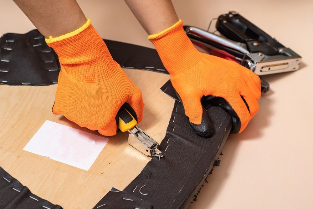 A Person Wearing Orange Gloves is Using a Stapler to Staple a Piece of Fabric — Furniture & Auto Pride in Macksville, NSW