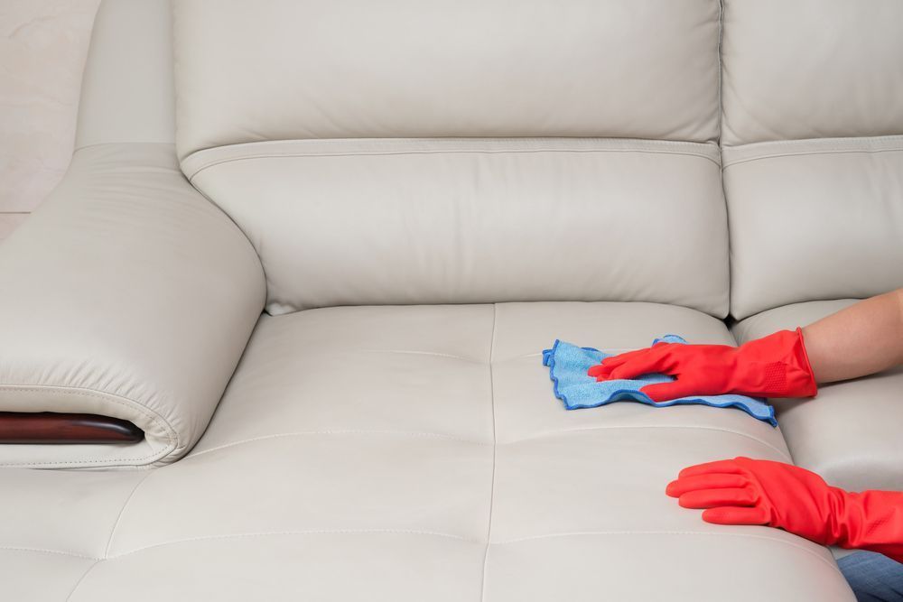 A Person Wearing Red Gloves is Cleaning a White Leather Couch With a Cloth — Furniture & Auto Pride in Macksville, NSW