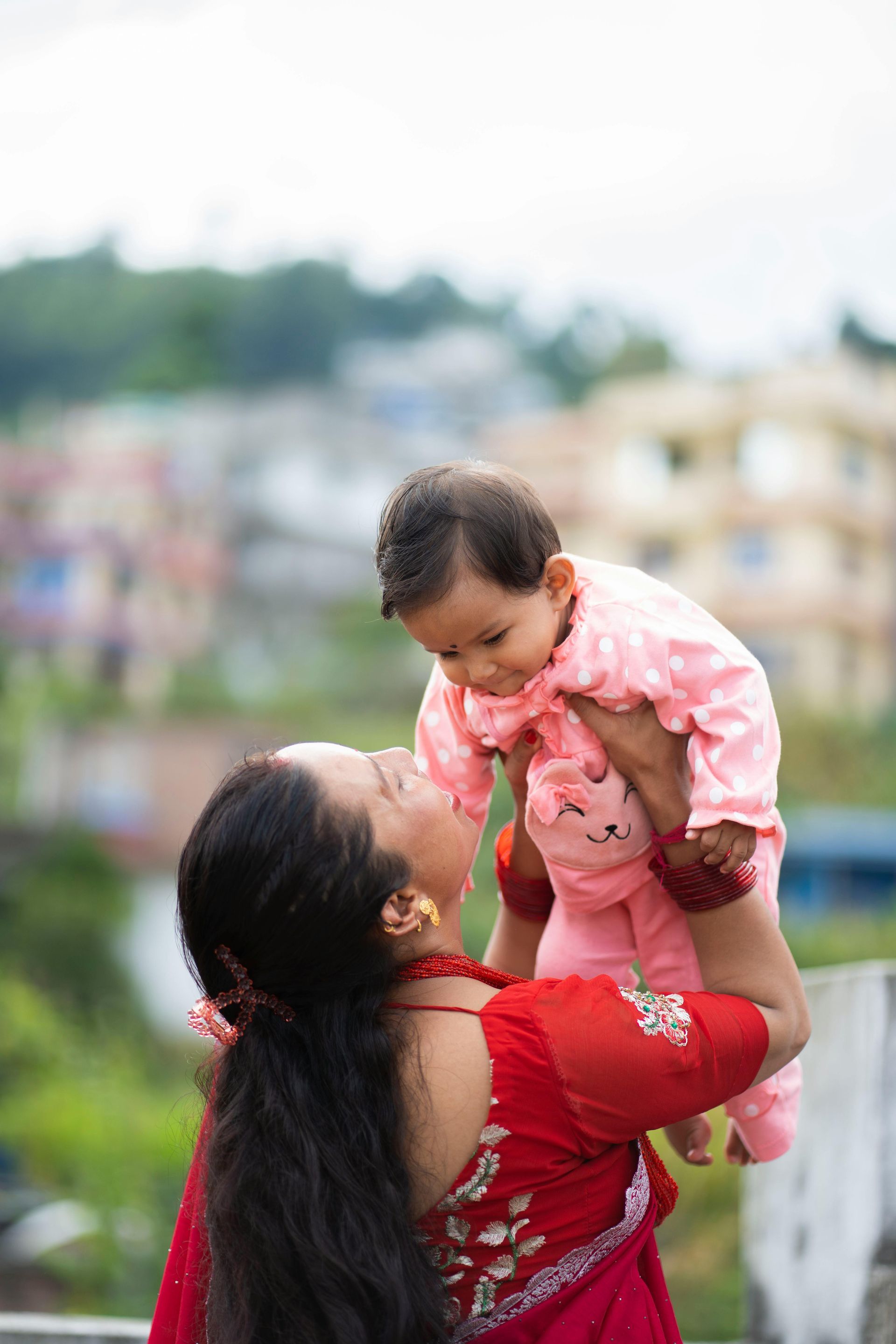 Woman holding her child in the air. She is outside with buildings in background.