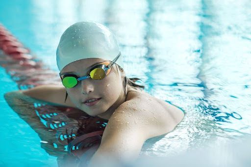 Girl in pool with goggles and cap.