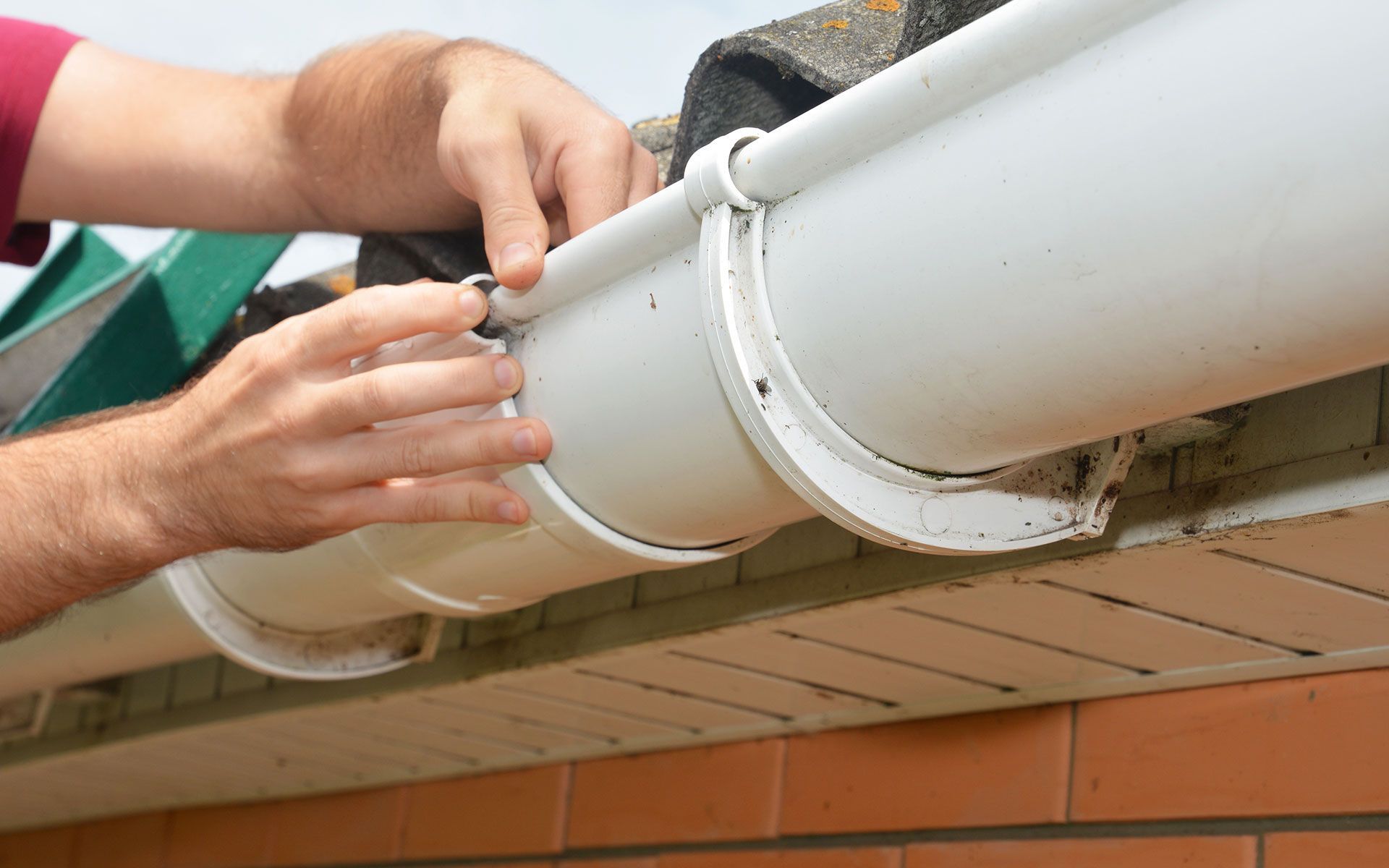 Person installing a white gutter on a brick building.