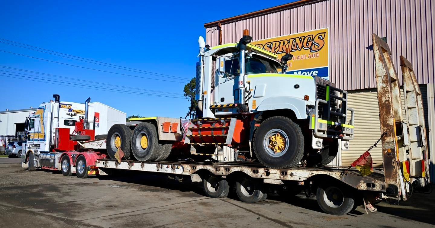 White tractor on a flatbed trailer outside a freight building under a clear blue sky