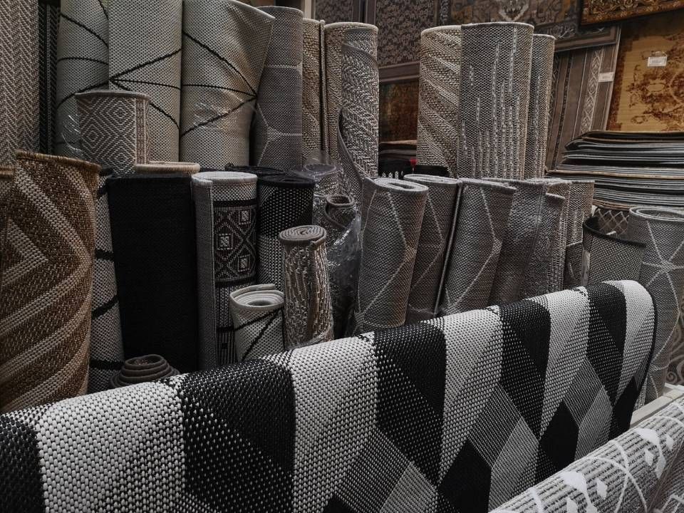 Stacked rugs and carpets in a showroom, with black-and-white patterned rolls in front.