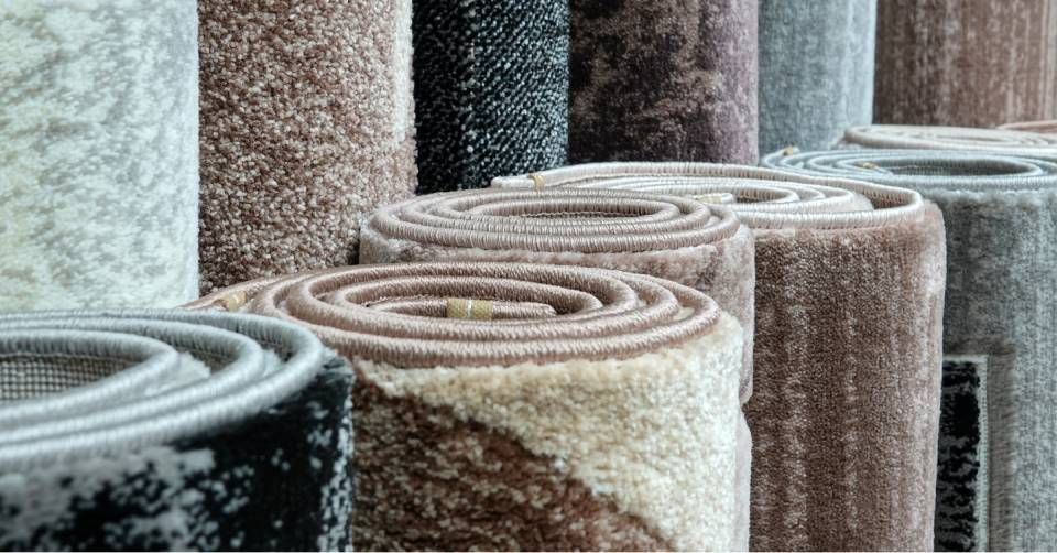 Rolled rugs in various neutral colors stacked in a row, seen from above.