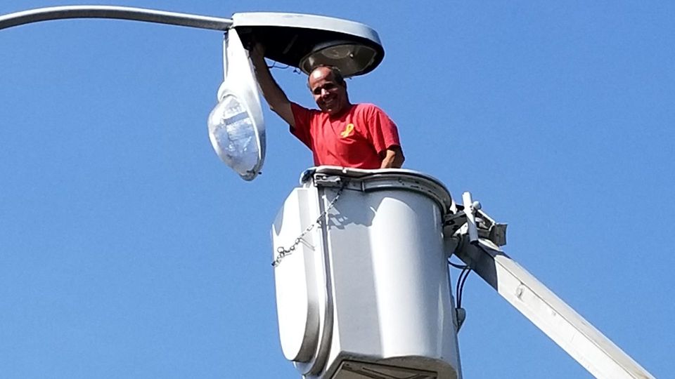 A man in a red shirt is working on a street light