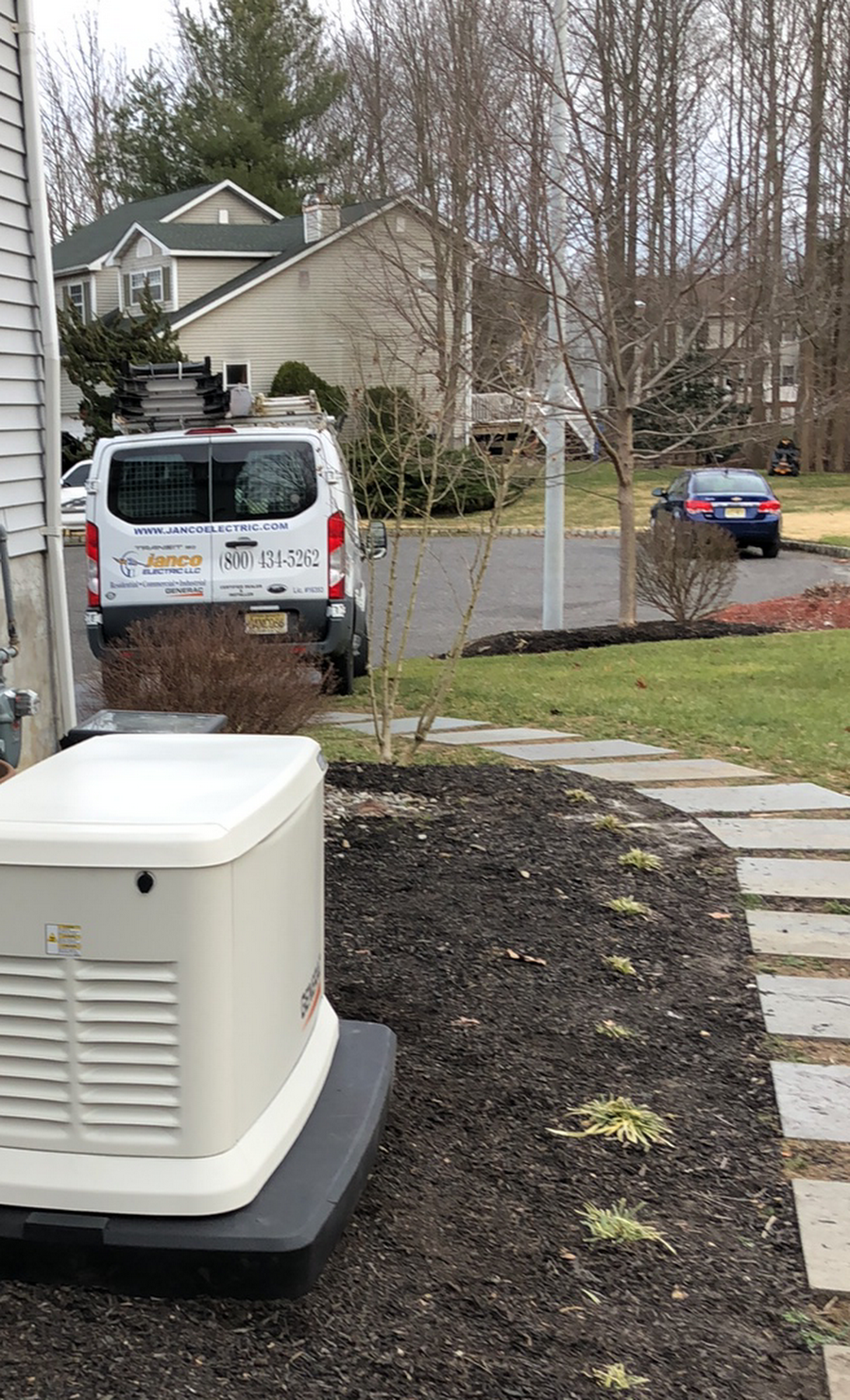 A white van is parked in front of a house next to a generator.