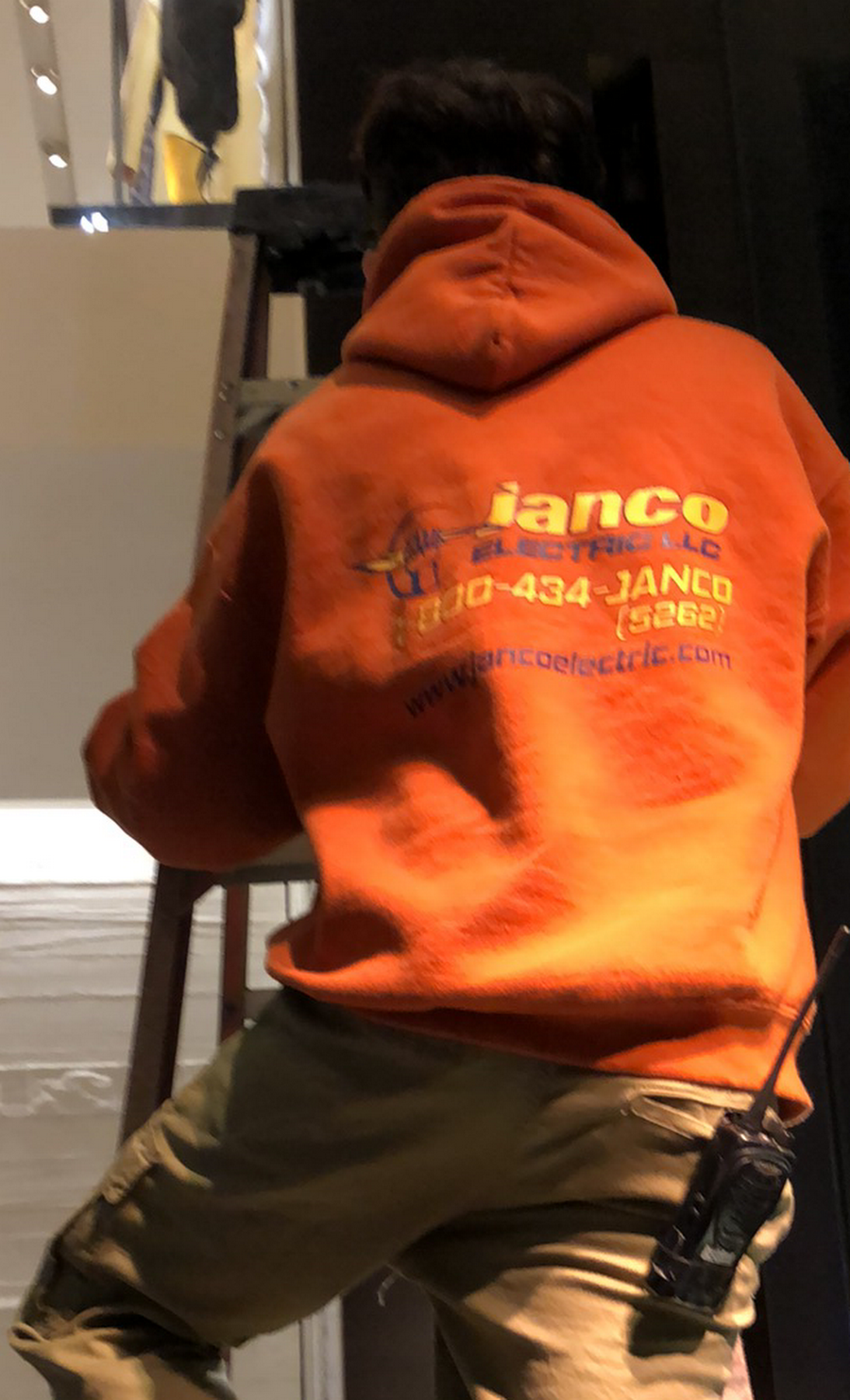 A man wearing an orange lanco hoodie stands on a ladder