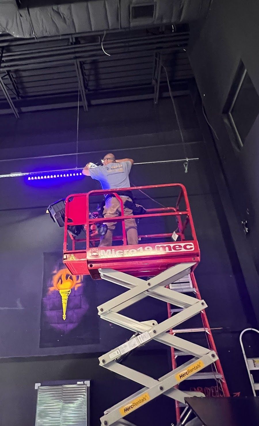 A man is standing on a scissor lift in a dark room.