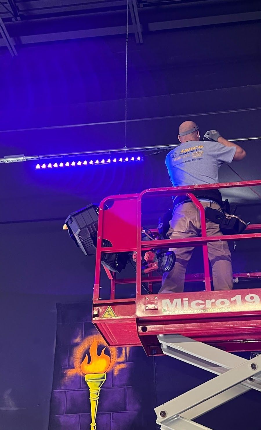 A man is standing on a scissor lift working on a ceiling.