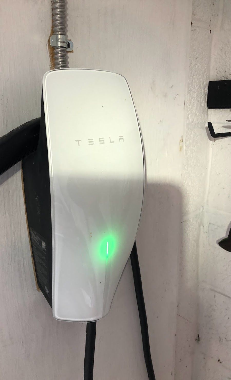 A tesla charger is plugged into a wall and has a green light on it.