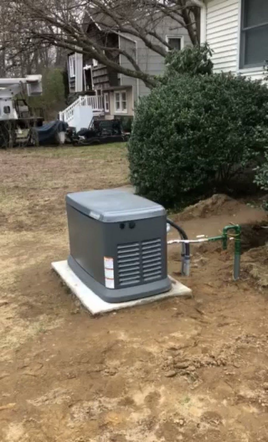 A generator is sitting in the dirt in front of a house.
