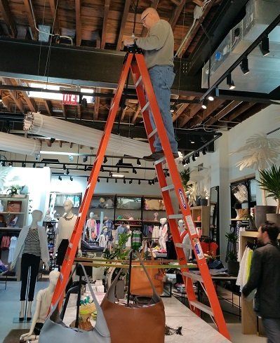A man is standing on an orange ladder in a store