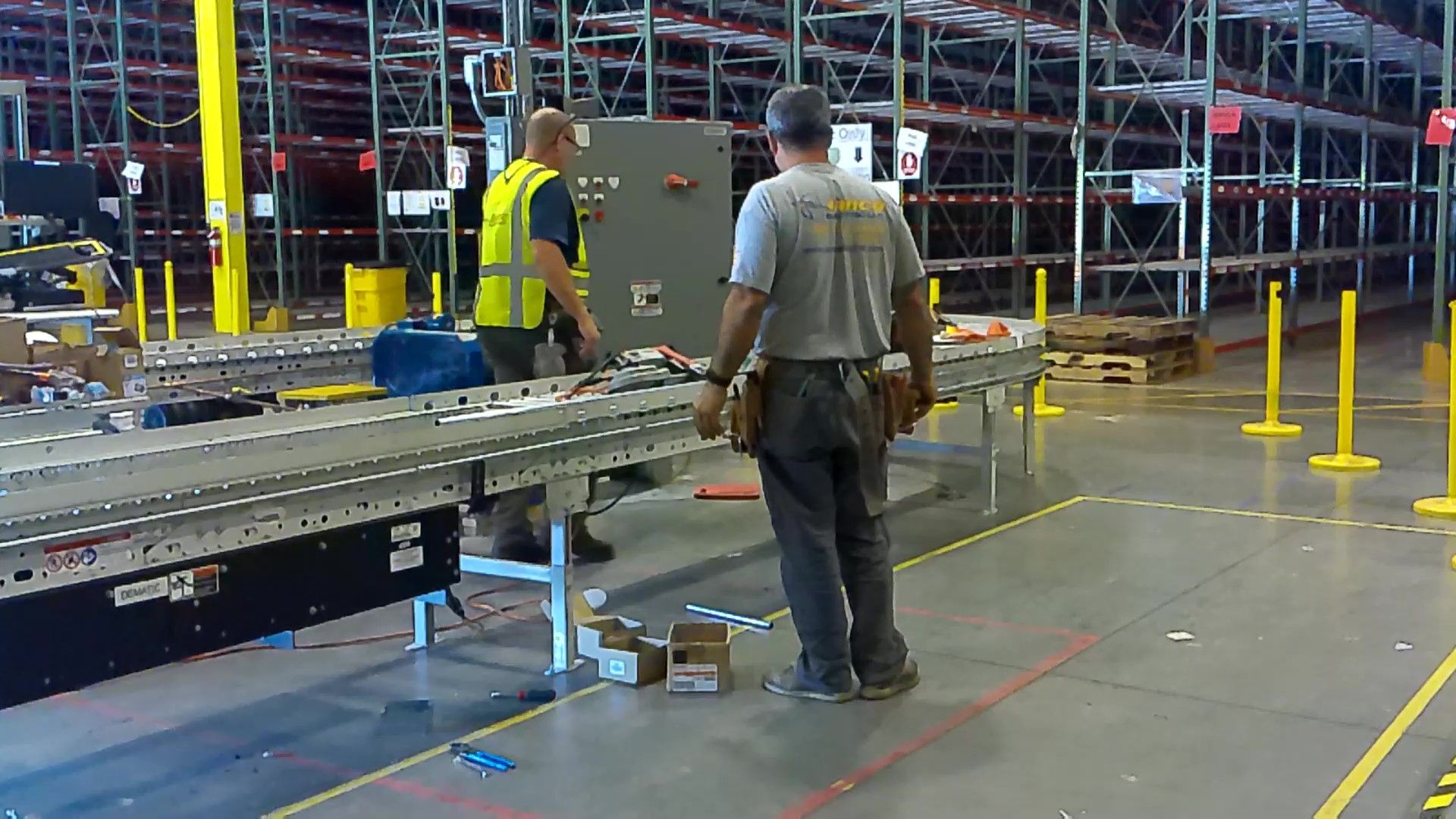 Two men are working on a conveyor belt in a warehouse.