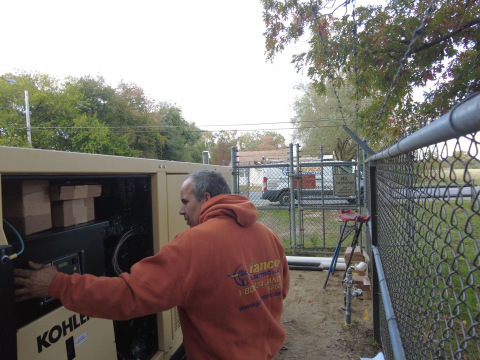 A man is working on a generator in front of a chain link fence.