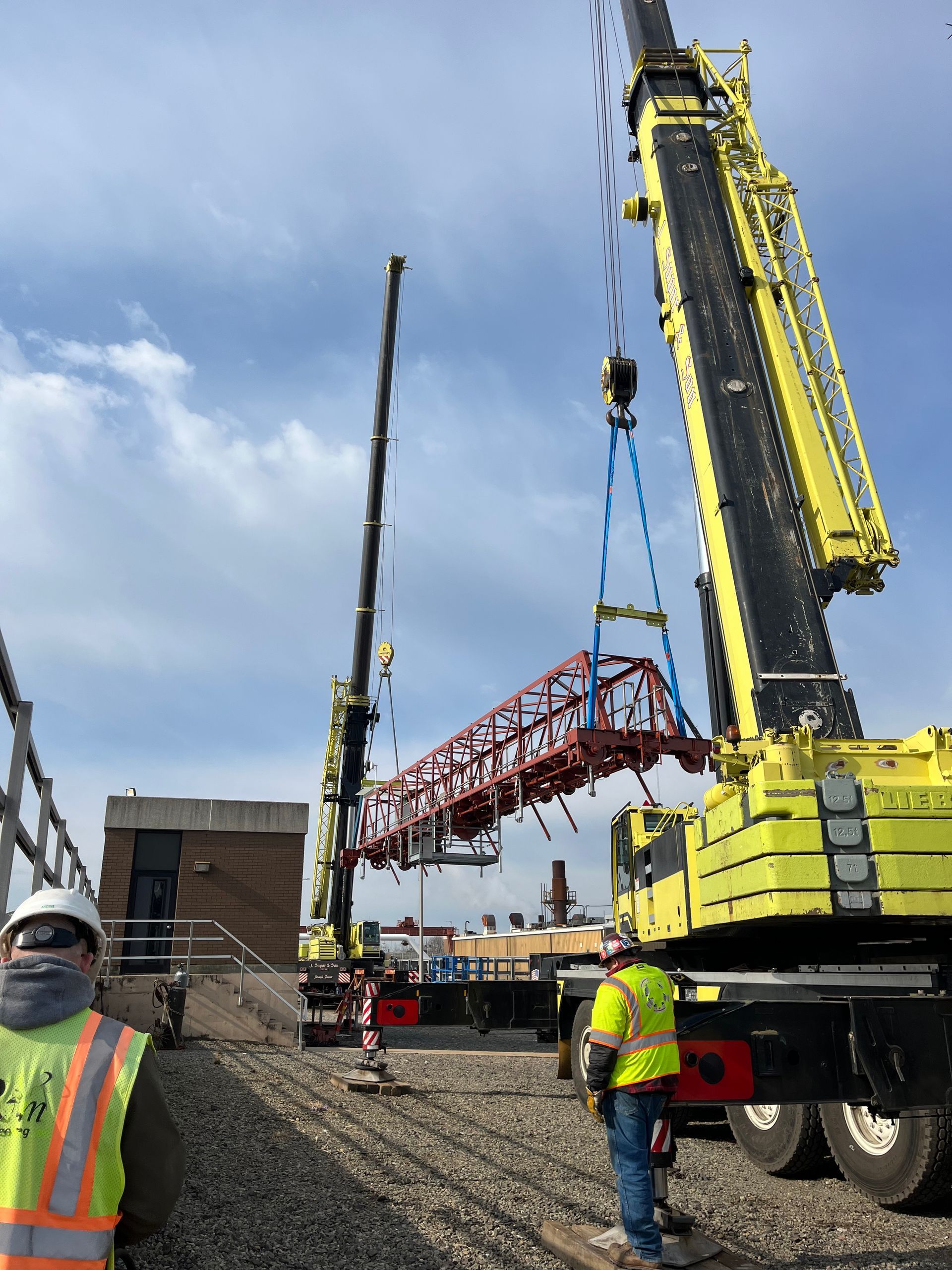 A construction worker is standing in front of a large yellow crane
